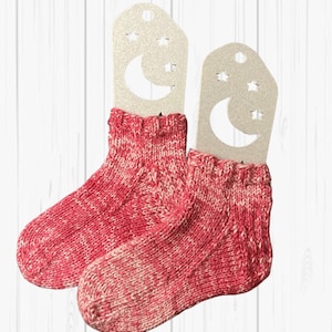 Peut inclure: Une paire de chaussettes en tricot rouge et blanc avec un motif de lune et d'étoiles sur les étiquettes.
