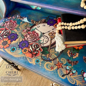 May include: A blue painted table top with a decorative design featuring a large pocket watch, flowers, butterflies, and a key. The design is in a vintage style with gold accents. The table top is also decorated with a lace pattern and a paisley pattern. The text "LOVE BY CHERI re:design" is visible in the bottom left corner of the image.