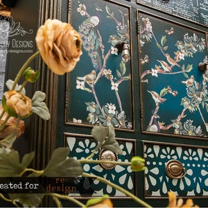 Peut inclure: Un cabinet bleu sarcelle avec des garnitures dor&eacute;es orn&eacute;es et des motifs floraux et d'oiseaux d&eacute;coratifs. Le cabinet a plusieurs tiroirs avec des motifs d&eacute;coup&eacute;s complexes et des boutons en m&eacute;tal. Le texte "LOTUS THEORY DESIGNS" et "www.lotustheorydesigns.com" est visible sur le cabinet.