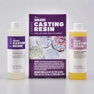 May include: A casting resin kit with two bottles labeled "Side A" and "Side B", and a purple box. The bottles contain clear and yellow liquids. The box reads "Amazing Casting Resin" and "Cures and turns white in 10 minutes".