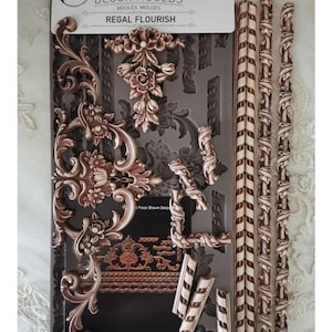 May include: A package of decorative molds labeled "DECOR MOULDS REGAL FLOURISH". The molds are in a dark gray color and feature ornate, floral, and scrollwork designs. The package also includes several long, decorative pieces. The dimensions are 5" x 10".