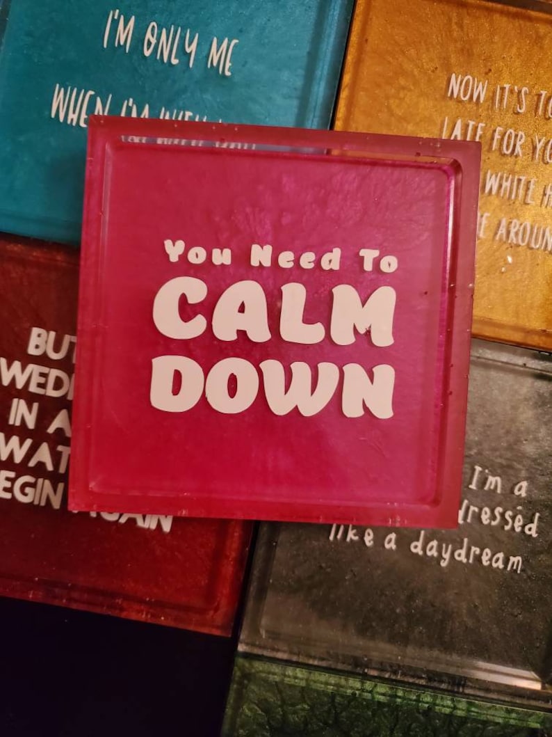 May include: Pink square coaster with the text "You Need To Calm Down" in white letters. The coaster has a glittery finish.