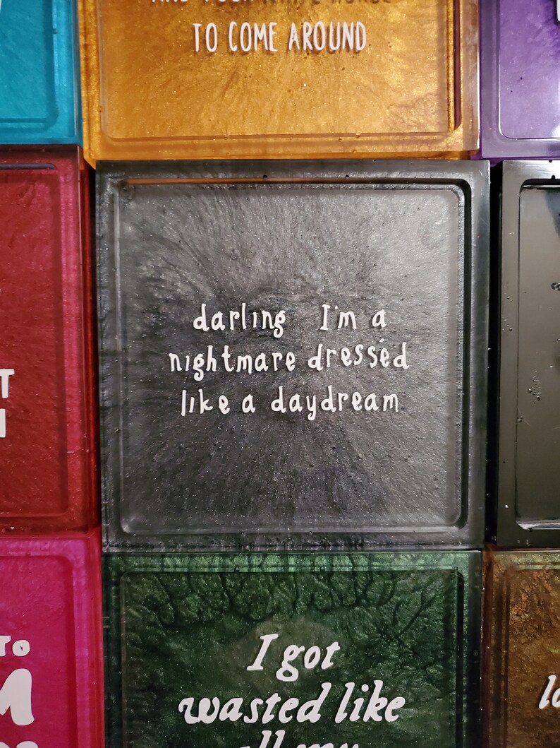 May include: Three square glass tiles with black frames. The tiles have a glittery background and white text. The top tile says "TO COME AROUND". The middle tile says "darling I'm a nightmare dressed like a daydream". The bottom tile says "I got wasted like".