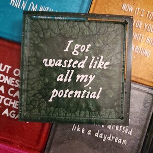 May include: A green glass coaster with white text that reads "I got wasted like all my potential like a daydream".