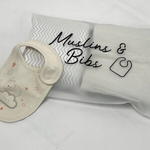 May include: A set of baby essentials, including a bib and muslin cloths, packaged in a clear bag. The bib is beige with a cute cloud and bear design. The bag is labeled "Muslins & Bibs".