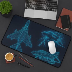 May include: A black desk mat with a blue wireframe design of fighter jets. The design includes three jets, with one appearing to be struck by lightning. A white mouse sits on the mat.