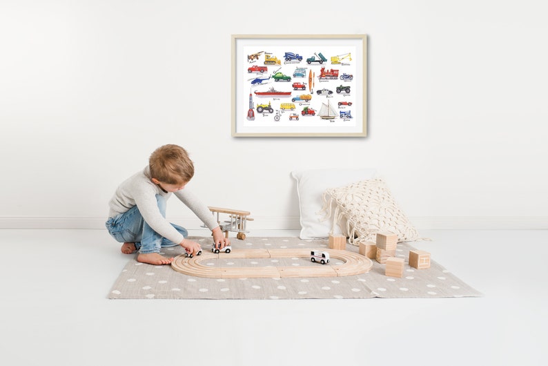 May include: A young child plays with toy cars and a wooden airplane on a gray and white rug. A framed print of a colorful illustration of various vehicles hangs on the wall behind the child.