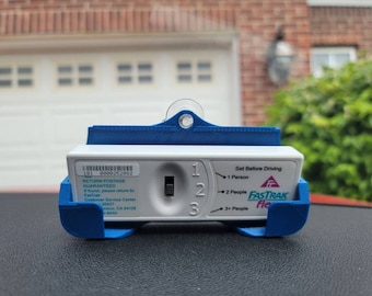 Puede incluir: Un transpondedor Fastrak Flex blanco con un soporte de plástico azul. El transpondedor tiene una pequeña pantalla con los números 1, 2 y 3, y el texto "Set Before Driving" y "1 Person", "2 People", y "3+ People".