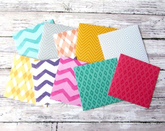 May include: Nine patterned paper squares in various colors and designs, including yellow, pink, green, blue, and gray. The squares are arranged in a staggered pattern.