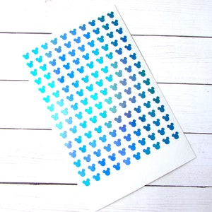 May include: A sheet of stickers featuring a pattern of small, blue Mickey Mouse head shapes. The stickers transition in color from light turquoise to deep blue. The sheet is on a white background.