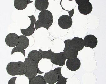 May include: A collection of black and white paper circles scattered on a white background. The circles are of varying sizes and are arranged in a random pattern.
