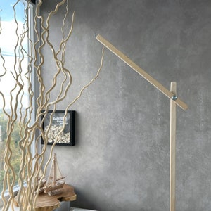 Può includere: Un supporto per mobile in legno con un braccio lungo che si estende lateralmente. Il supporto è in legno naturale e ha un design semplice. Il supporto è montato su una superficie bianca.