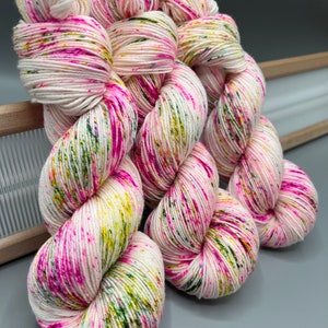May include: Three skeins of yarn in a white base with pink, green, and yellow speckles. The yarn is twisted into a spiral shape.