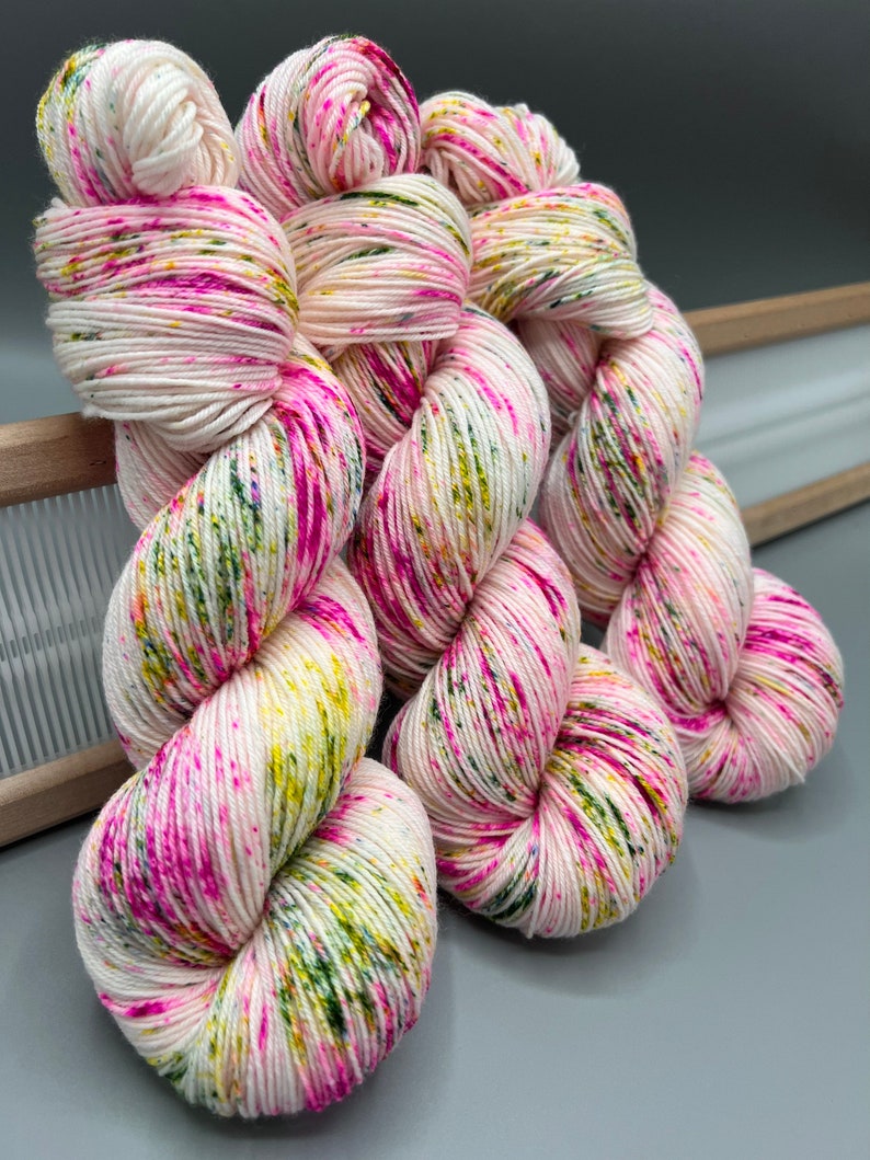 May include: Three skeins of yarn in a white base with pink, green, and yellow speckles. The yarn is twisted into a spiral shape.