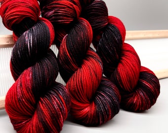 Könnte beinhalten: Drei Knäuel Garn in einer rot-schwarzen Farbkombination. Das Garn ist ein Feinstrickgarn und hat einen dezenten Melange-Effekt.