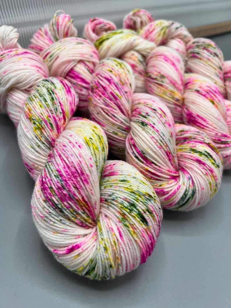 May include: A skein of white yarn with pink, green, and yellow speckles. The yarn is soft and fluffy, and it would be perfect for knitting or crocheting.