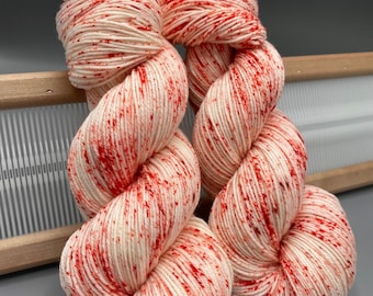 May include: Two skeins of white yarn with red speckles. The yarn is arranged in a loose, twisted shape.