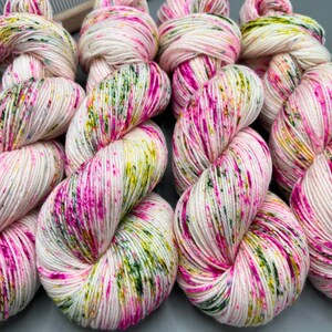 May include: Four skeins of yarn in a white base with pink, green, and yellow speckles. The yarn is arranged in a row, with each skein twisted into a loop.
