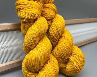 Puede incluir: Dos ovillos de hilo amarillo brillante, enrollados en bolas, se muestran sobre una superficie gris. El hilo es suave y esponjoso, y sería perfecto para tejer o hacer ganchillo.