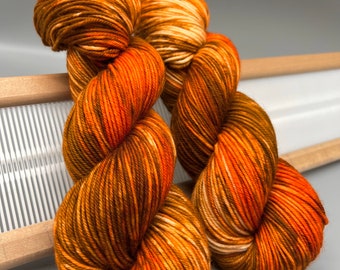May include: Two skeins of yarn in a brown, orange, and cream colorway. The yarn is arranged in a loose knot.
