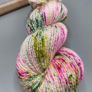May include: A skein of yarn in a white base with pink, green, and yellow speckles and a silver shimmer.