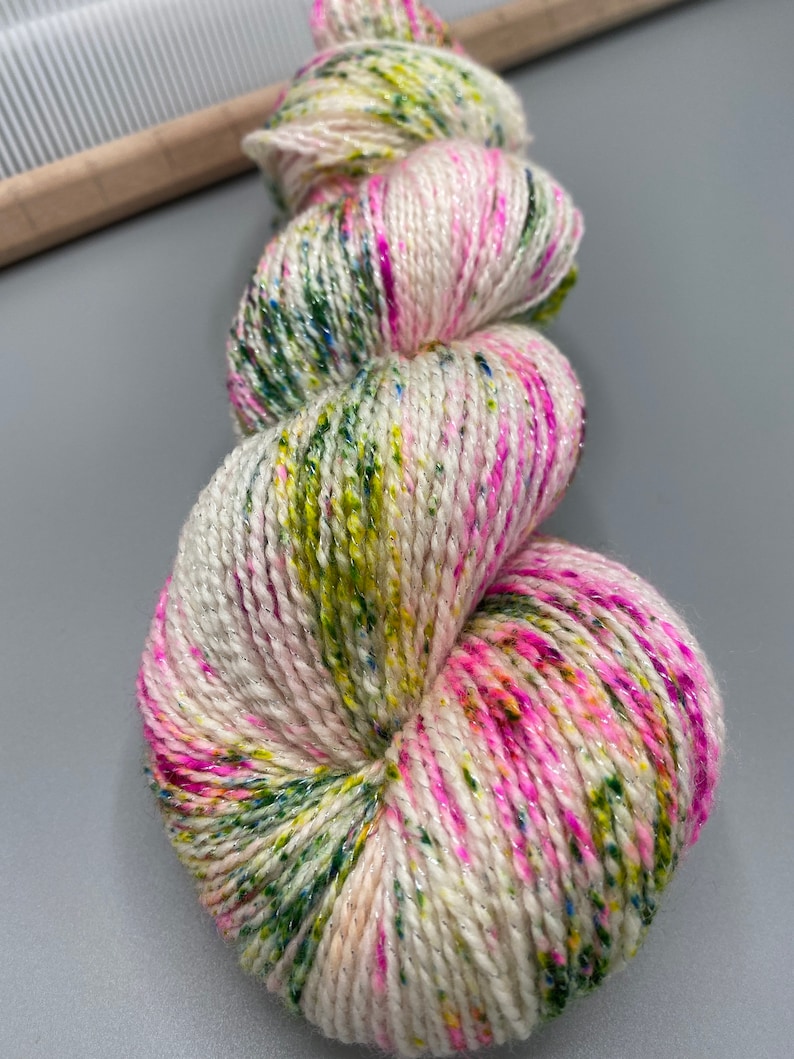 May include: A skein of yarn in a white base with pink, green, and yellow speckles and a silver shimmer.