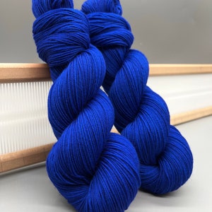 May include: Two skeins of bright blue yarn, wound into balls, are displayed on a wooden surface.