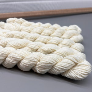 May include: Close-up of a white woven wall hanging made with yarn. The hanging has a textured, woven pattern.