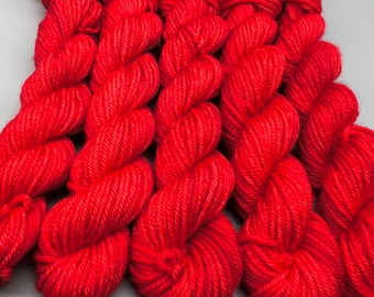 May include: Close-up of several skeins of vibrant red yarn. The yarn is tightly wound, showing the texture of the fibers. The bright red color is consistent throughout the skeins, suggesting a dyed product. The yarn is likely for knitting or crochet projects.