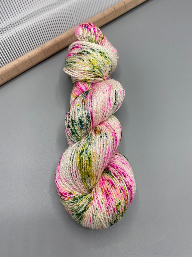 May include: A skein of yarn in a white base with speckles of pink, green, and yellow.