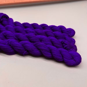 May include: A close-up of a skein of deep purple yarn. The yarn is soft and fluffy, and it is perfect for knitting or crocheting.