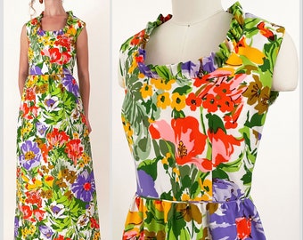 May include: A white maxi dress with a colorful floral print. The dress has a square neckline with a ruffled trim and sleeveless straps. The print features large flowers in shades of red, orange, yellow, purple, and green.