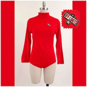 May include: Red long-sleeved turtleneck bodysuit with a small "Off Limits" patch on the front.