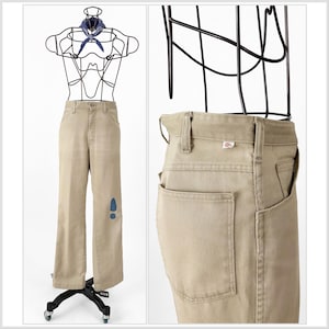 May include: Khaki-colored pants with a wide leg design. The pants are displayed on a wire mannequin with a blue bandana. A blue footprint design is on the left leg. The back of the pants shows a pocket and a small logo.