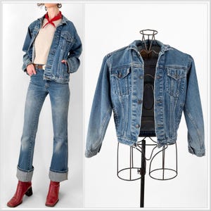 May include: A light blue denim jacket with button closures and pockets. The jacket is displayed on a metal form and worn with matching jeans and red boots. The jeans have a flared leg and are cuffed at the bottom.