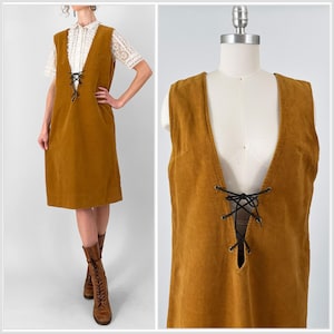 May include: A mustard yellow corduroy dress with a deep V-neck and lace-up detail. The dress is sleeveless and has a straight silhouette.