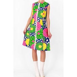 May include: A sleeveless knee-length dress featuring a vibrant floral pattern in shades of bright green, hot pink, and yellow against a dark blue background. The dress includes a vertical white lace trim detail running down the center front.
