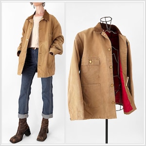 May include: A tan work jacket with a brown corduroy collar and button closure. The jacket has two front pockets and is lined with red fabric. The jacket is displayed on a mannequin and worn by a person.