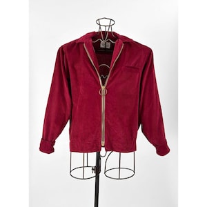 May include: A burgundy corduroy jacket with a gold zipper and a small pocket on the left side.