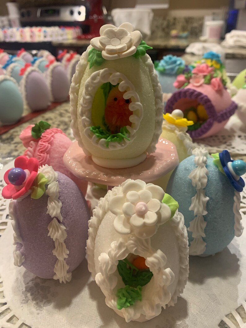 May include: A collection of decorated Easter eggs. The eggs are white, purple, and blue with various pastel-colored decorations, including flowers, birds, and nests.