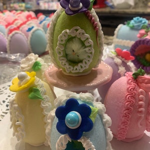 May include: A collection of decorated Easter eggs with various colors and designs. The eggs are made of sugar and have intricate details, including flowers, lace, and a small bird.