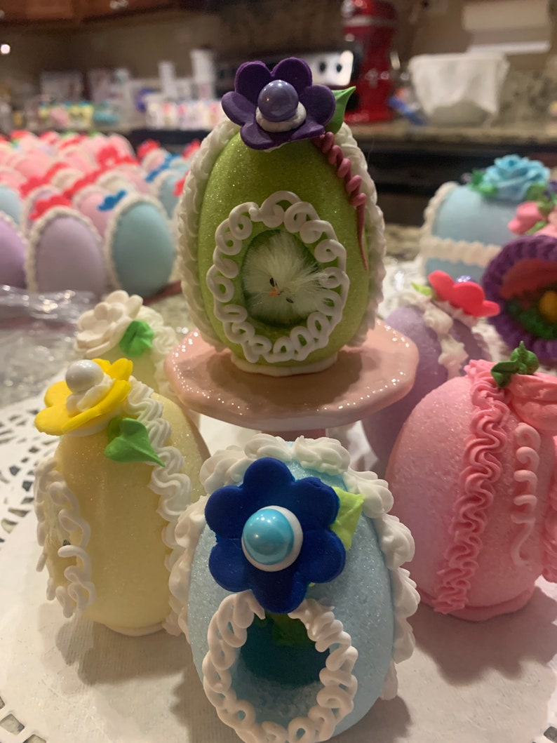 May include: A collection of decorated Easter eggs with various colors and designs. The eggs are made of sugar and have intricate details, including flowers, lace, and a small bird.