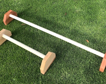 May include: Two wooden parallel bars with white painted metal bars. The bars are set up on a green artificial grass surface.