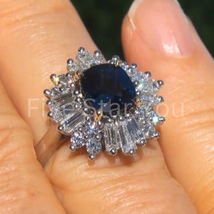 Puede incluir: Un anillo de plata con un gran zafiro ovalado azul oscuro rodeado por un halo de diamantes más pequeños. El anillo tiene un diseño floral delicado.