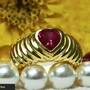 May include: A gold ring with a heart-shaped ruby gemstone. The ring has a textured band with multiple ridges.