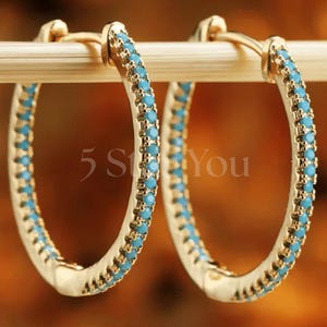 May include: Gold hoop earrings with a row of turquoise blue stones around the edge.