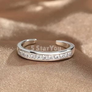 May include: A silver-toned ring with a row of clear, sparkling stones. The ring has an open design and the text "5 Star You" is visible. The ring is set against a neutral, warm-toned background.