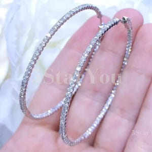 Può includere: Un paio di grandi orecchini a cerchio argentati con una fila di pietre di zircone cubico trasparenti attorno al bordo.