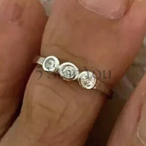 May include: A silver ring with three clear, round gemstones set in individual bezels. The ring is shown on a finger, with the text "555 You" visible.