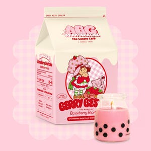 May include: A pink and white milk carton candle with a strawberry shortcake design. The candle is labelled "Berry Best" and "The World of Strawberry Shortcake". The candle is made with 100% soy wax.